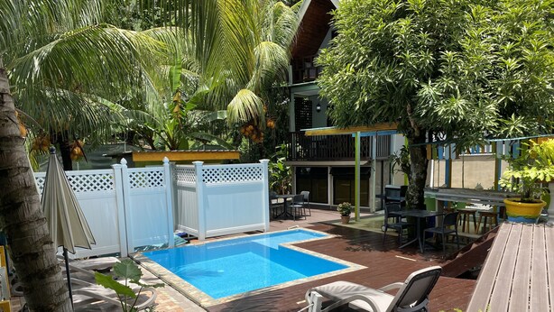 Patio con piscina, terraza de madera, sillones de descanso y plantas en macetas.