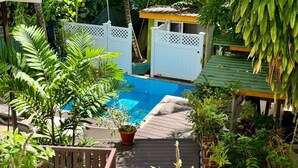 Una piscina rodeada de abundante vegetación, una terraza de madera y una pequeña estructura con techo.