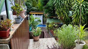 Un espacio al aire libre con suelo de piedra, plantas en macetas, una construcción pequeña y una piscina.