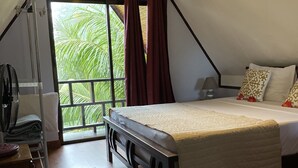 Un dormitorio con cama, mesita de noche, lámpara, ventilador y vista a zonas verdes a través de una ventana.