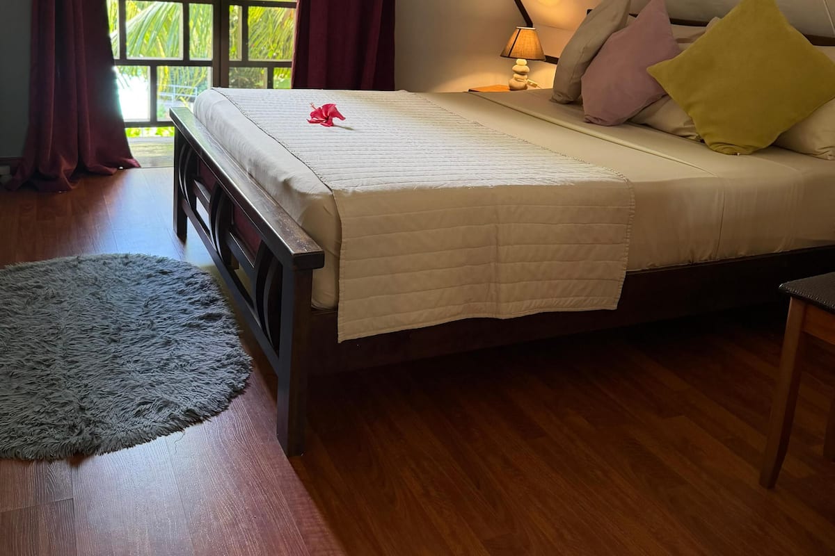 A bedroom with a bed, a nightstand, a lamp, and a view of greenery outside.