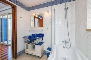A bathroom with a white bathtub, a blue sink, and a glass shower enclosure. - Villa Violet (Supetar)