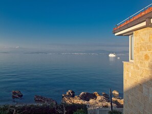 A coastal view with a large body of water, a distant shoreline, and a building with a tiled facade. - Villa Violet (Supetar)