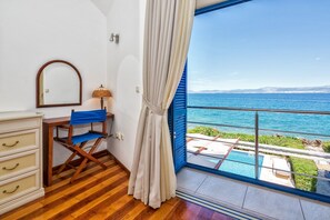 Une pièce avec un plancher en bois, un bureau avec une chaise, un miroir, une lampe et une grande fenêtre donnant sur la mer et une piscine.