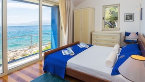 Ein Hotelzimmer mit einem großen Bett, einem Schreibtisch, einem Stuhl, einem Fenster mit Meerblick und einem Kleiderschrank.