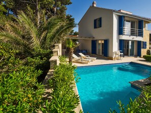 A poolside area with lounge chairs, a pool, and a building with blue shutters. - Villa Rosemary (Supetar)
