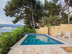 A swimming pool with a stone wall and two lounge chairs. - Villa Rosemary (Supetar)