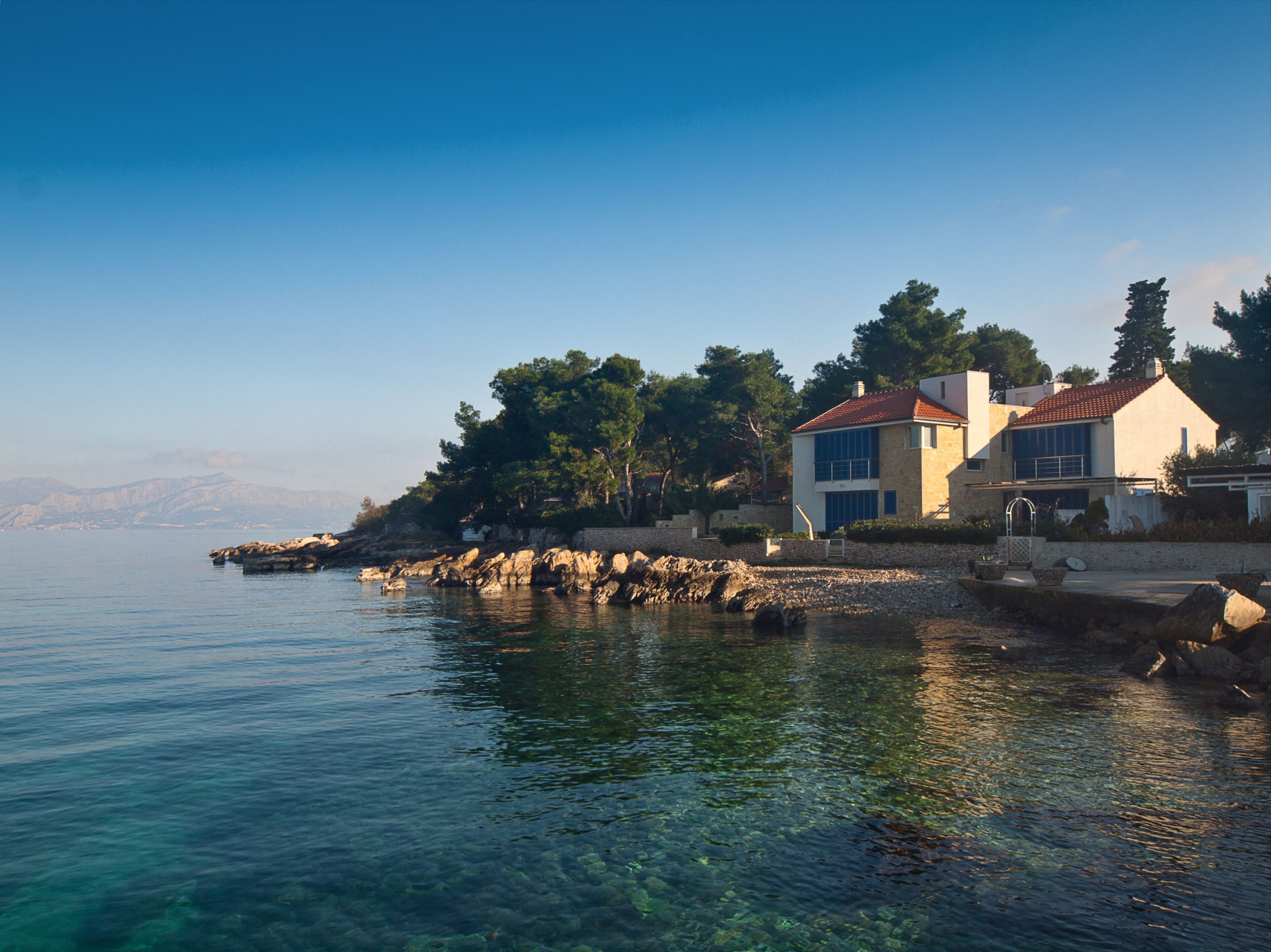 A coastal property with a clear view of the sea, a stone wall, and a building with a red roof.