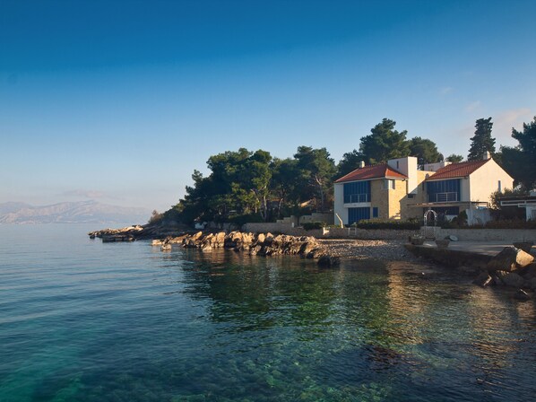 A coastal property with a clear view of the sea, a stone wall, and a building with a red roof. - Villa Rosemary (Supetar)