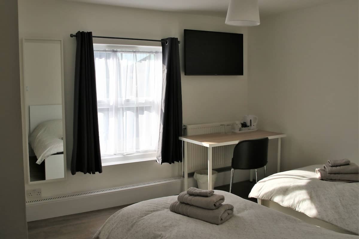 A hotel room with two beds, a desk, a chair, a TV, and a window with curtains.