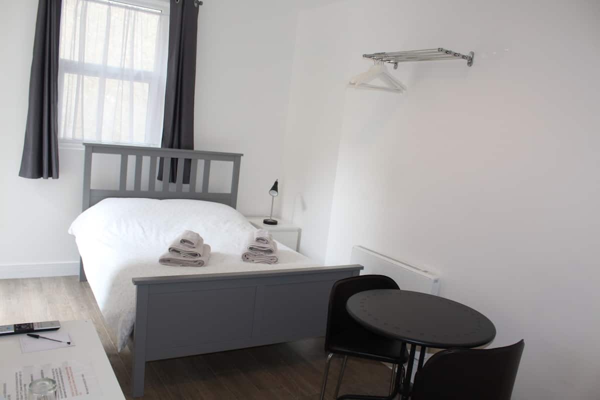 A neatly arranged bedroom with a bed, bedside table, chair, and a small table.