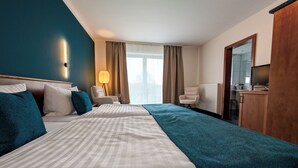 Quarto de hotel com cama, duas poltronas, uma escrivaninha, abajur e vista para o exterior.