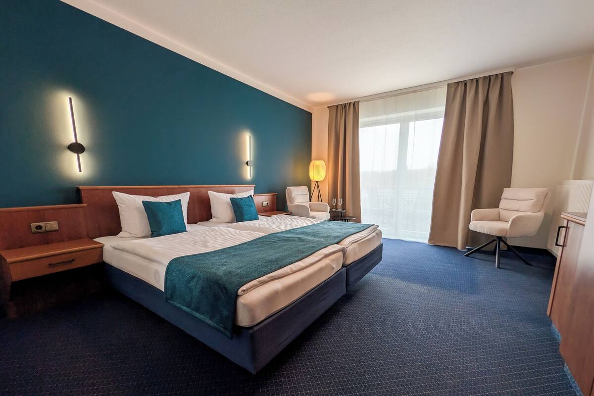 A hotel room with a large bed, bedside tables, a desk, a chair, and a window with curtains.