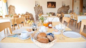 Uma área de refeições com mesas preparadas para o café da manhã, incluindo pão, ovos e bebidas.
