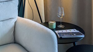 Um quarto com uma luminária, uma taça de vinho, uma vela e uma revista sobre uma mesa pequena.