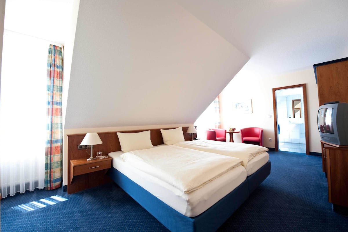 A hotel room with a large bed, a TV, a desk, and a red chair.