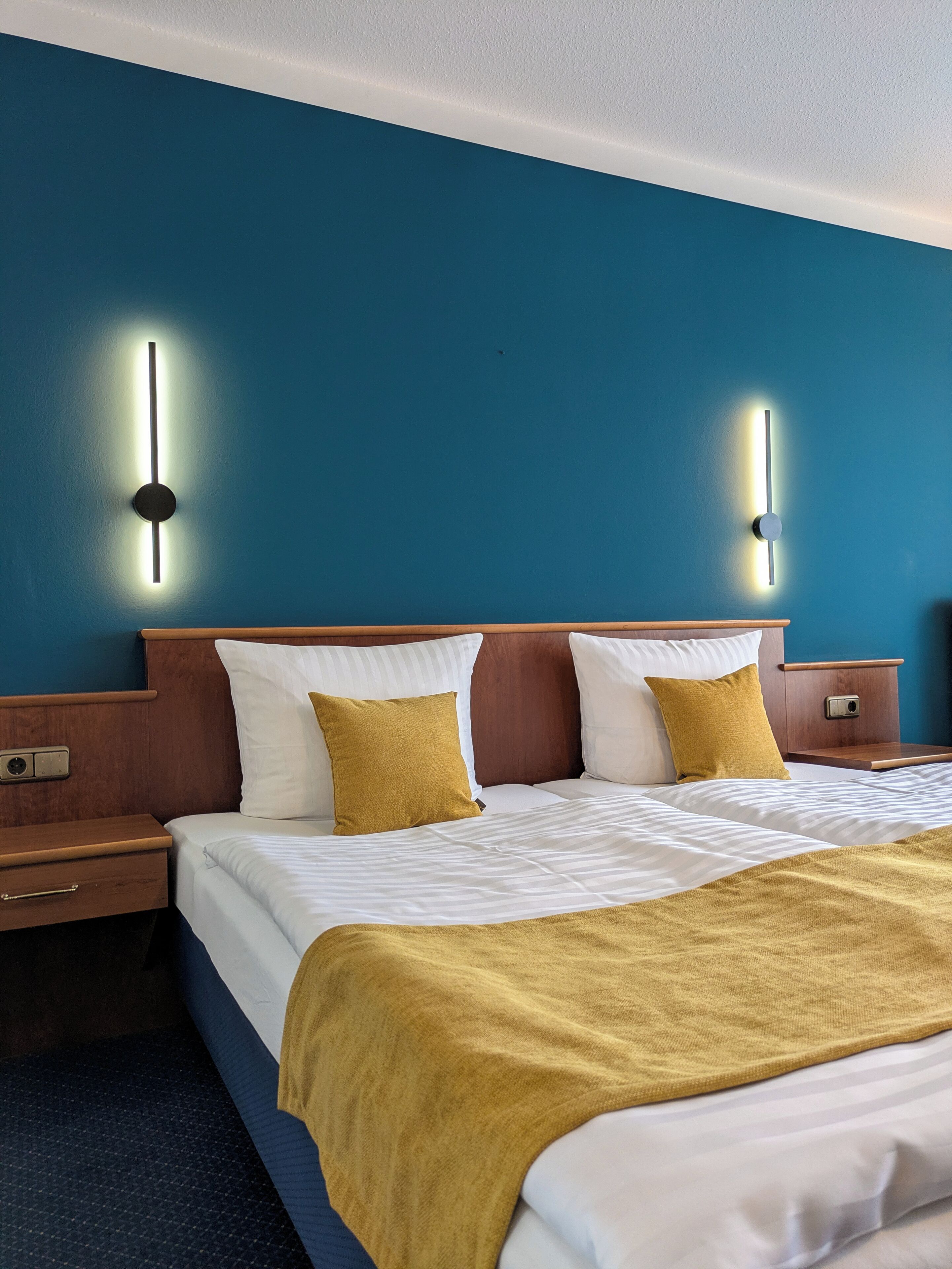 Una camera d'albergo con un letto, comodini e illuminazione a parete.