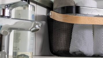 Un lavamanos con dispensador de jabón, una botella de jabón líquido y una cesta de malla con asa de madera.