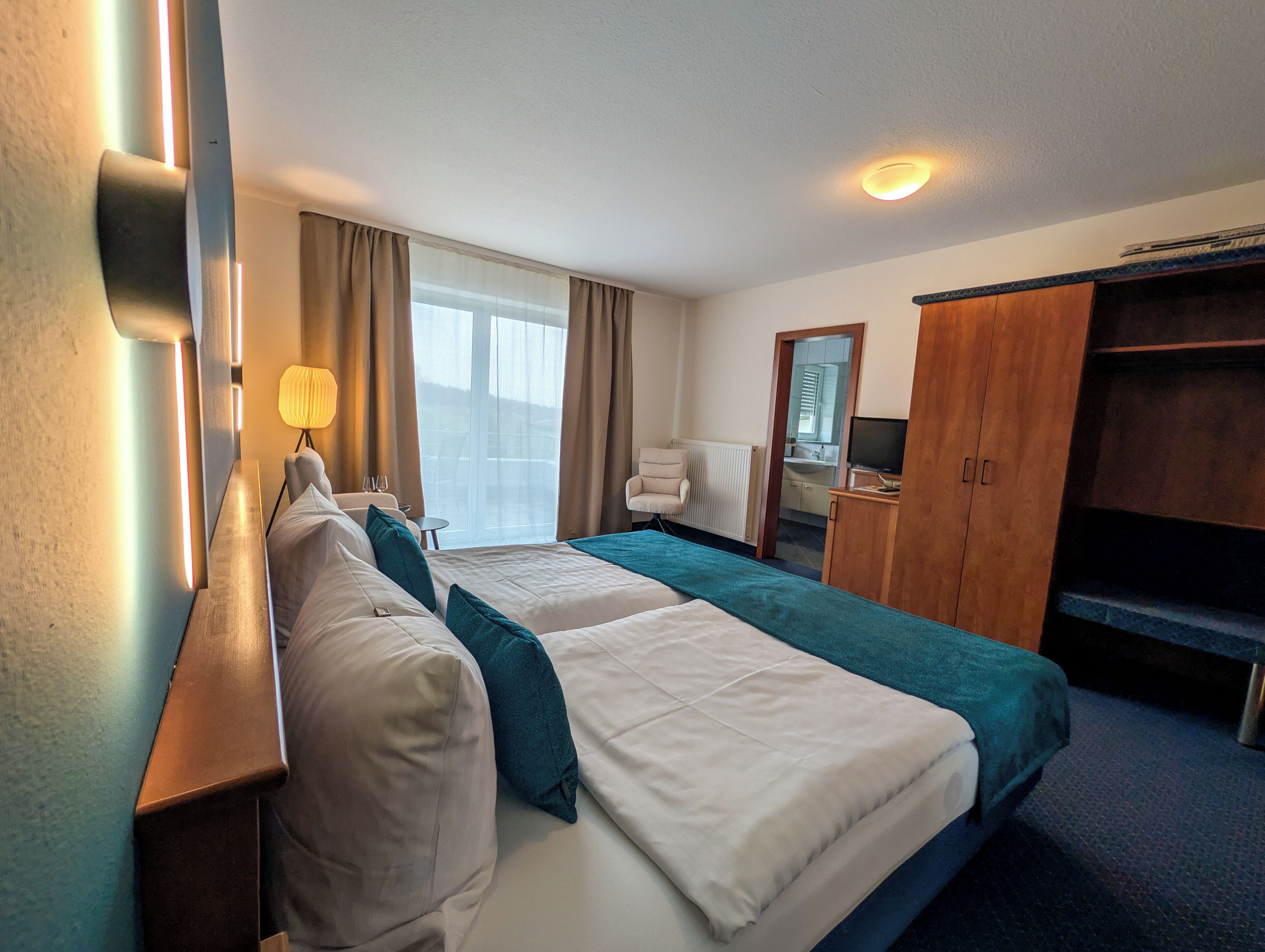 A hotel room with two beds, a desk, a chair, a TV, and a wardrobe.