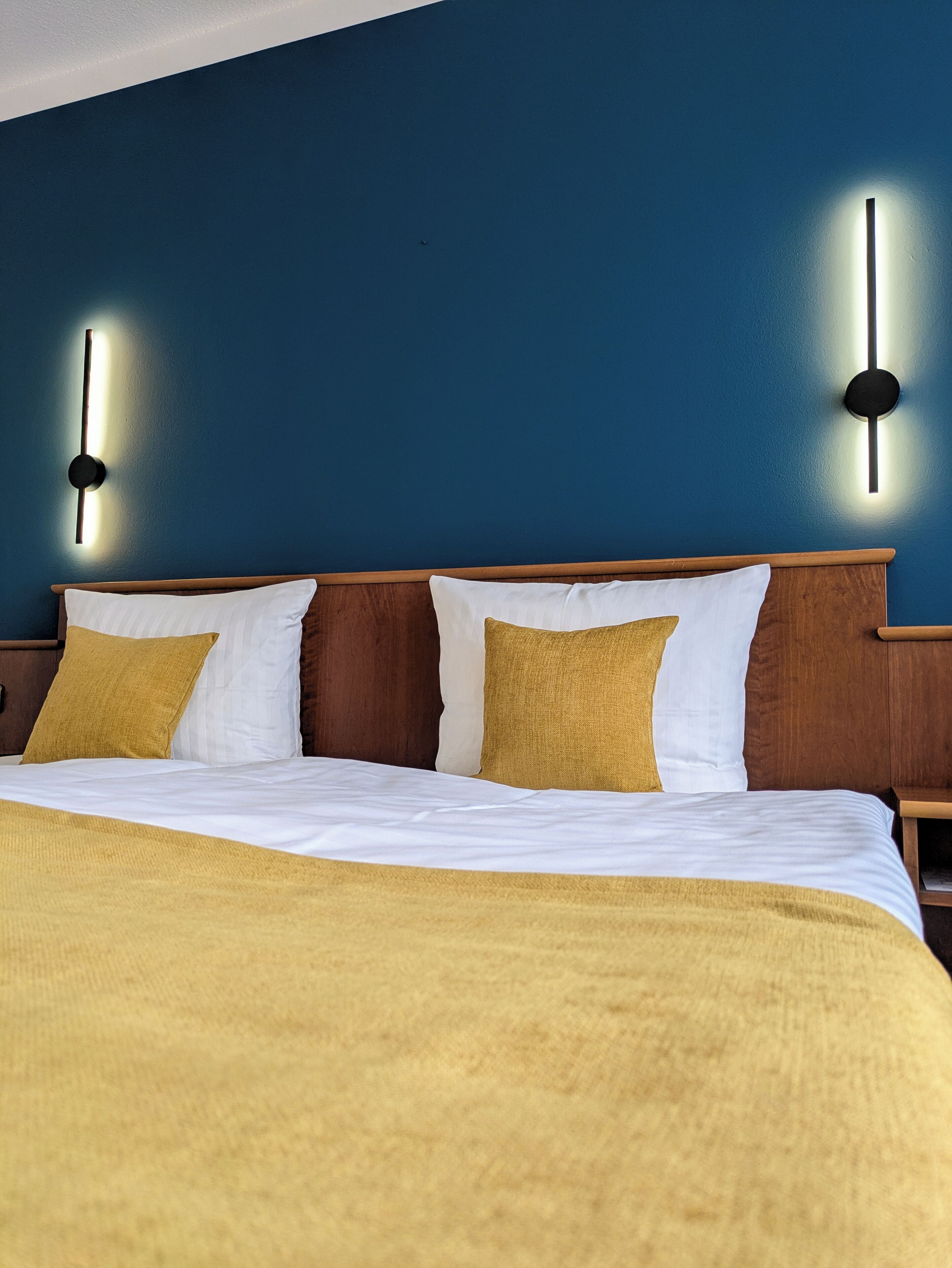 Habitación de hotel con cama, cabecero de madera, dos lámparas de pared y pared azul.