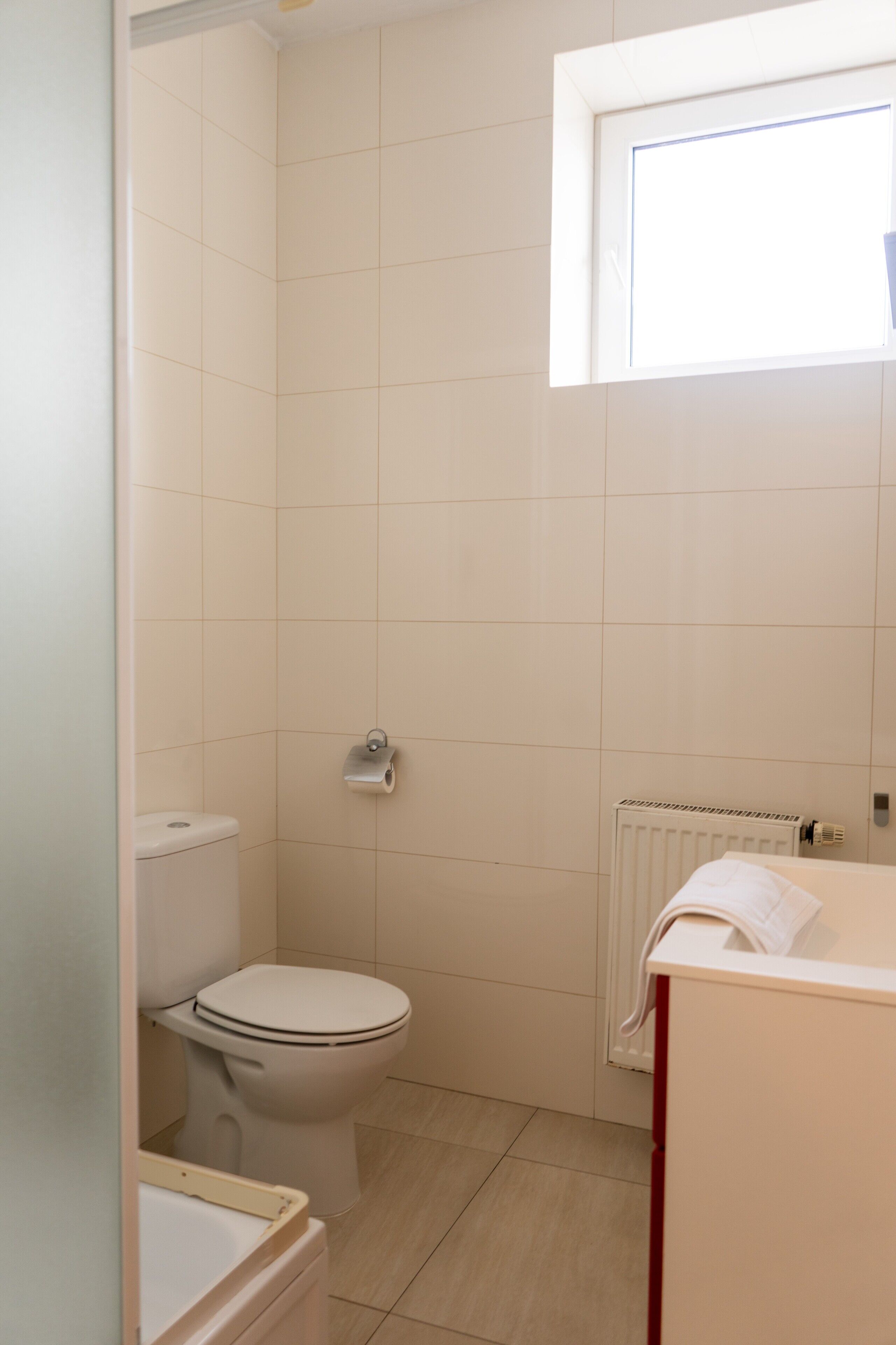 Een compacte badkamer met toilet, handdoekradiator en wastafel.