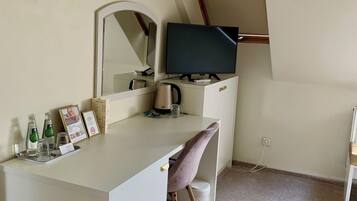 Quarto pequeno e moderno com uma escrivaninha branca, uma cadeira, uma cama e teto inclinado.