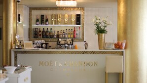 Zona de bar con un cartel de Moët & Chandon, estantes con diferentes botellas de licor, una máquina de café y un jarrón con flores.