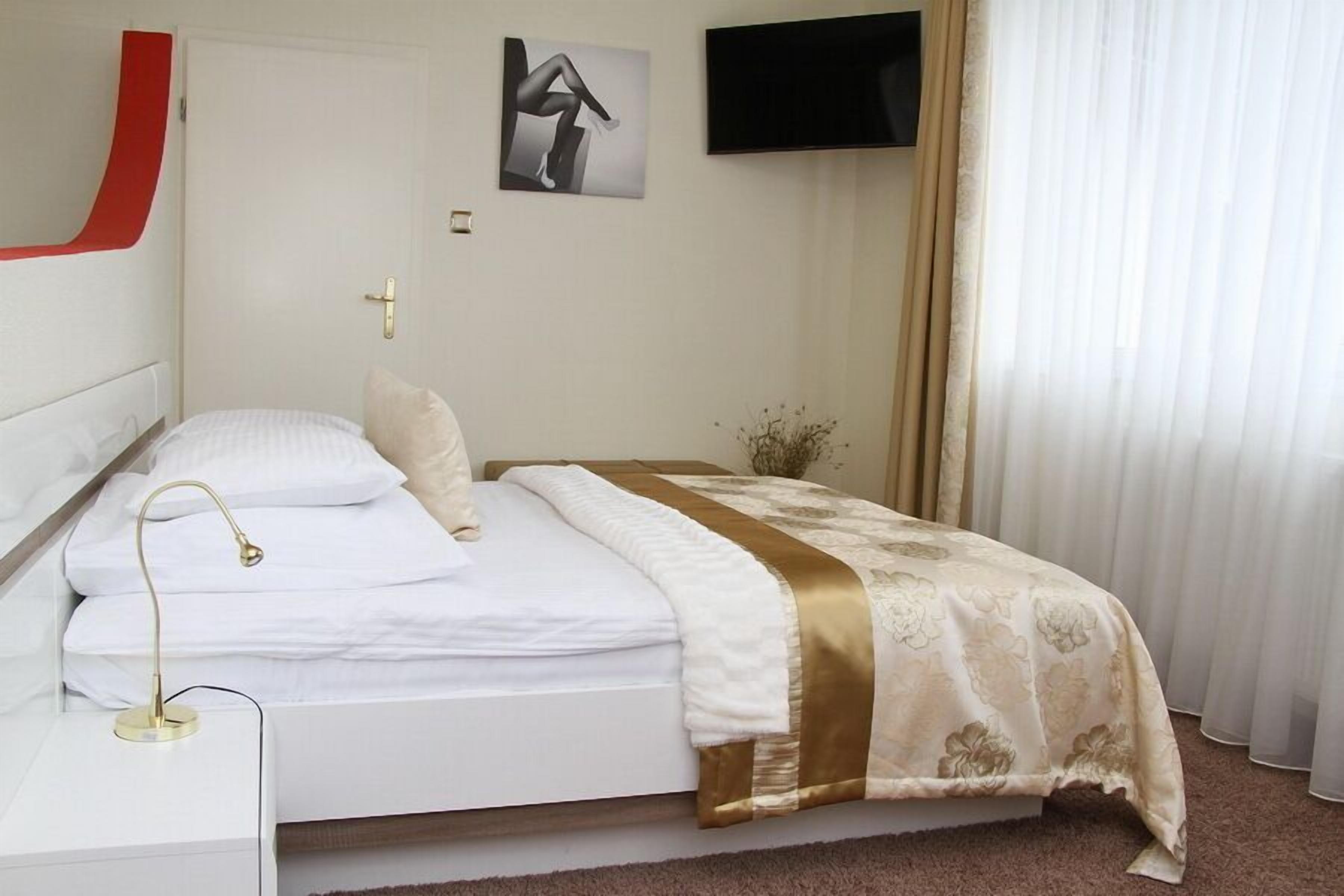 A neatly made bed with a white and gold bedspread, a bedside lamp, and a small potted plant.