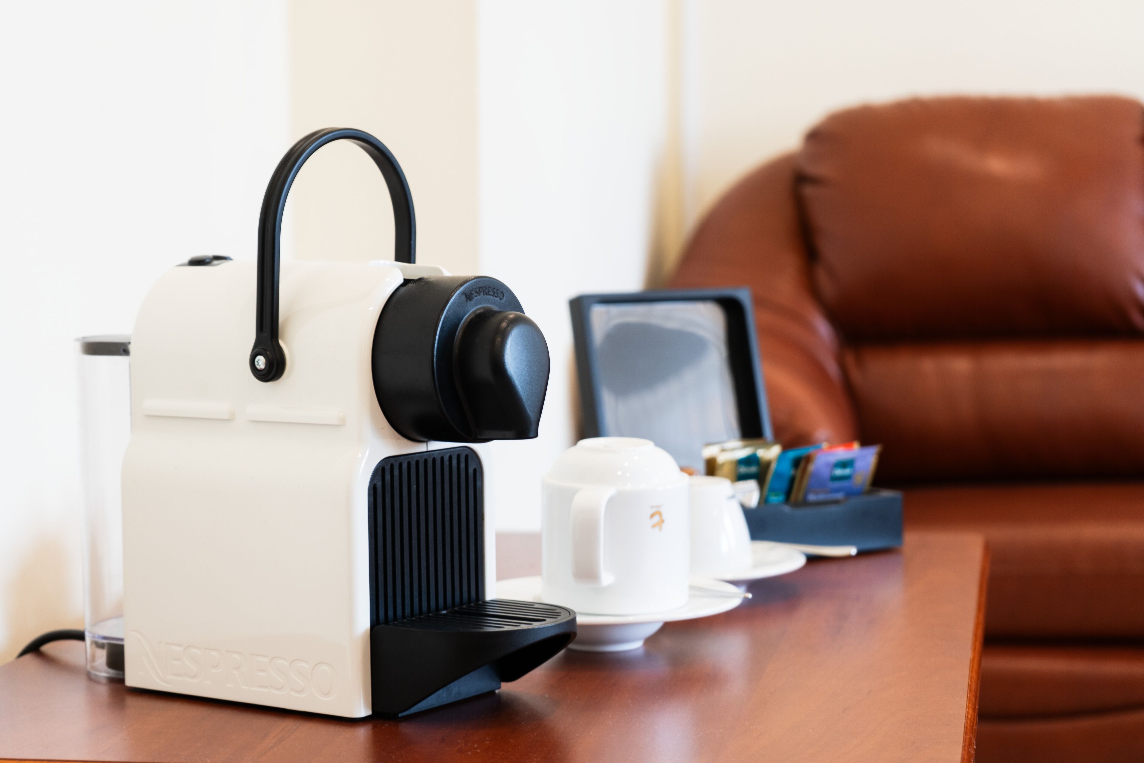 Een Nespresso koffiemachine op een houten tafel met een witte kop en schotel, een smartphone en een portemonnee.
