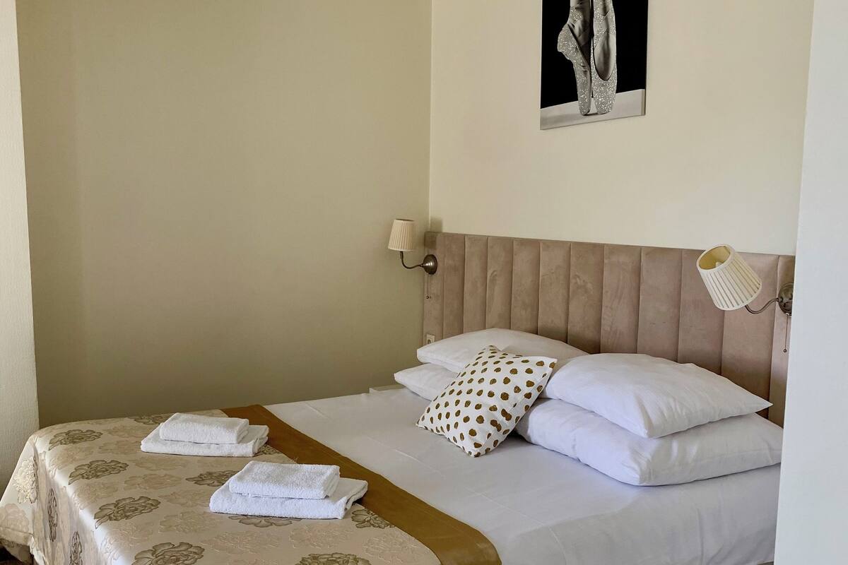 Una cama bien hecha con un edredón estampado con flores, almohadas blancas y un plaid marrón.
