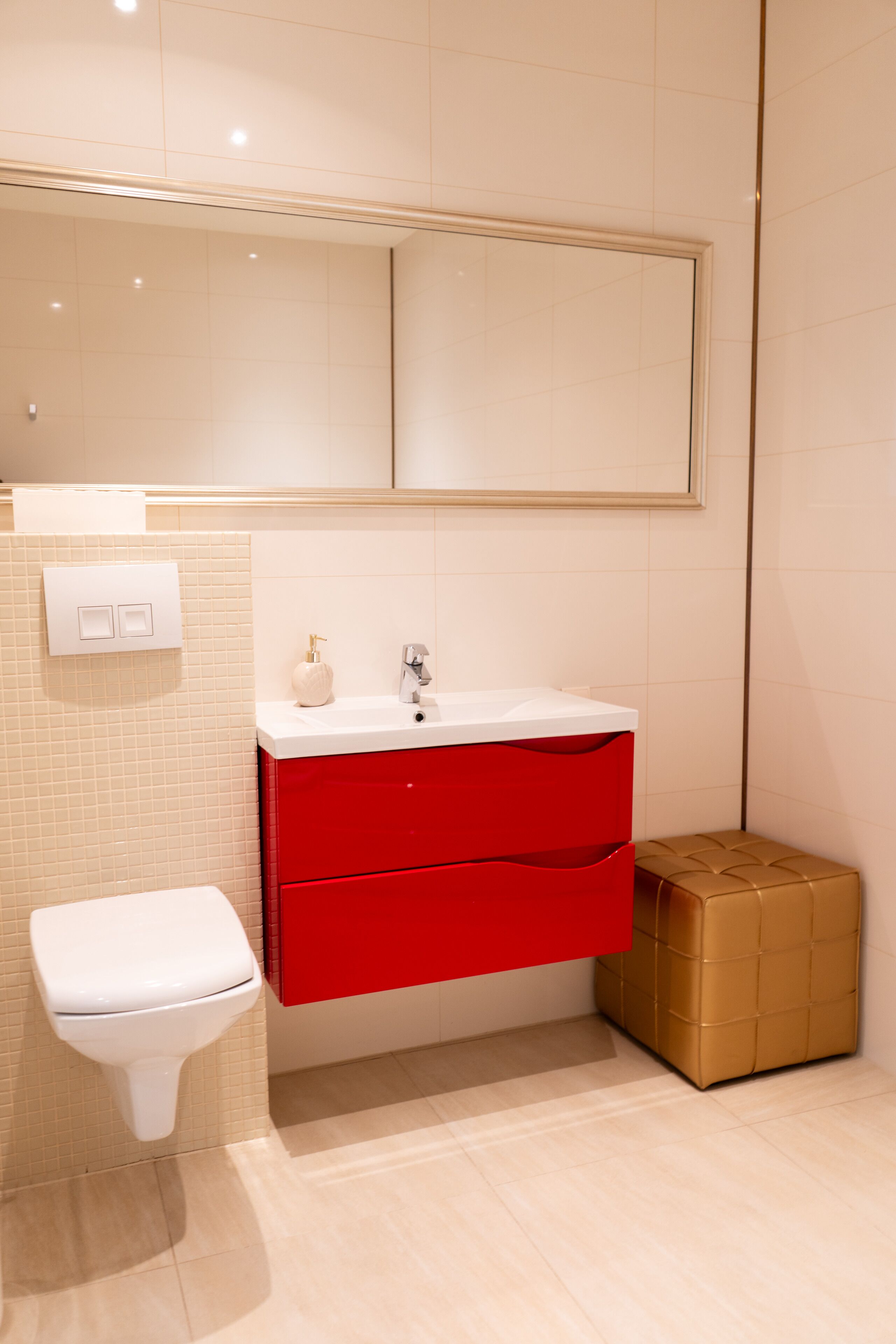 A bathroom with a white toilet, a red vanity, and a large mirror above the sink.