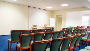 A conference room with a long table and rows of chairs, a whiteboard, and a projector screen.