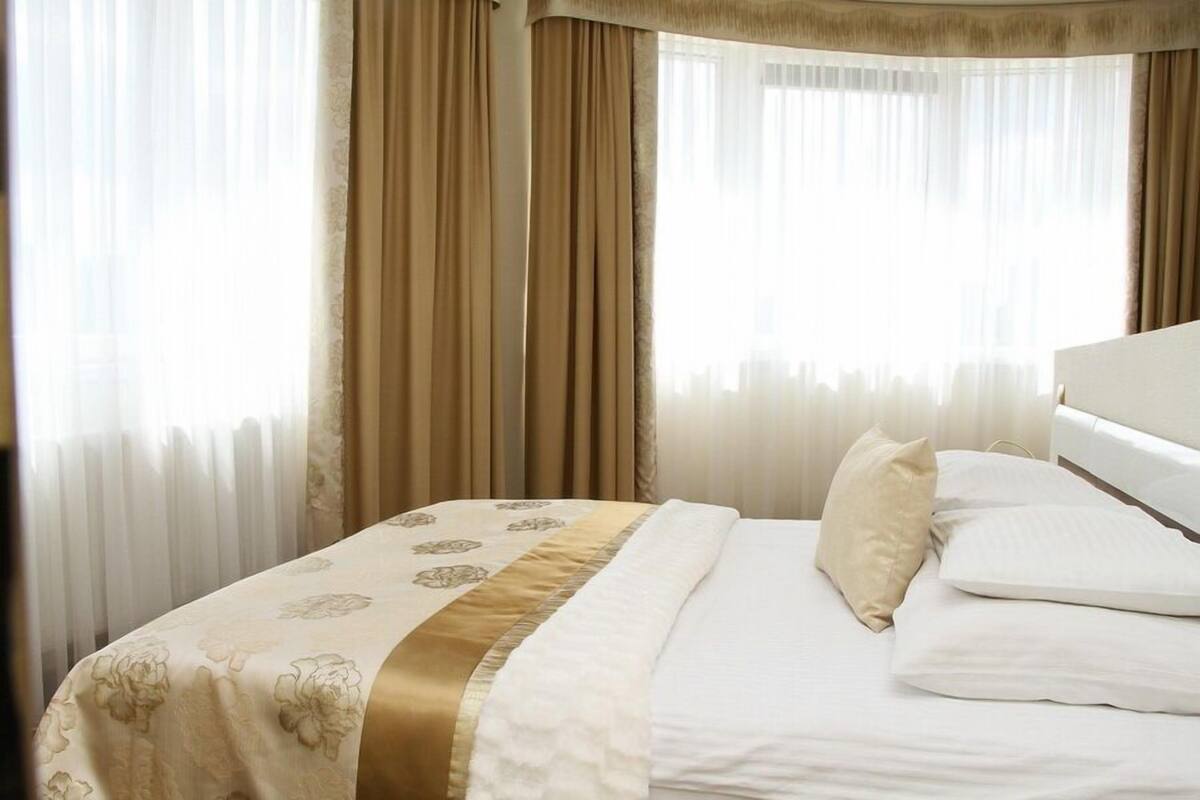 Una habitación de hotel con una cama, cortinas color beige y un cabecero blanco.