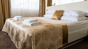 Una cama bien hecha con una colcha estampada con motivos florales, un cojín dorado y toallas dobladas al lado.