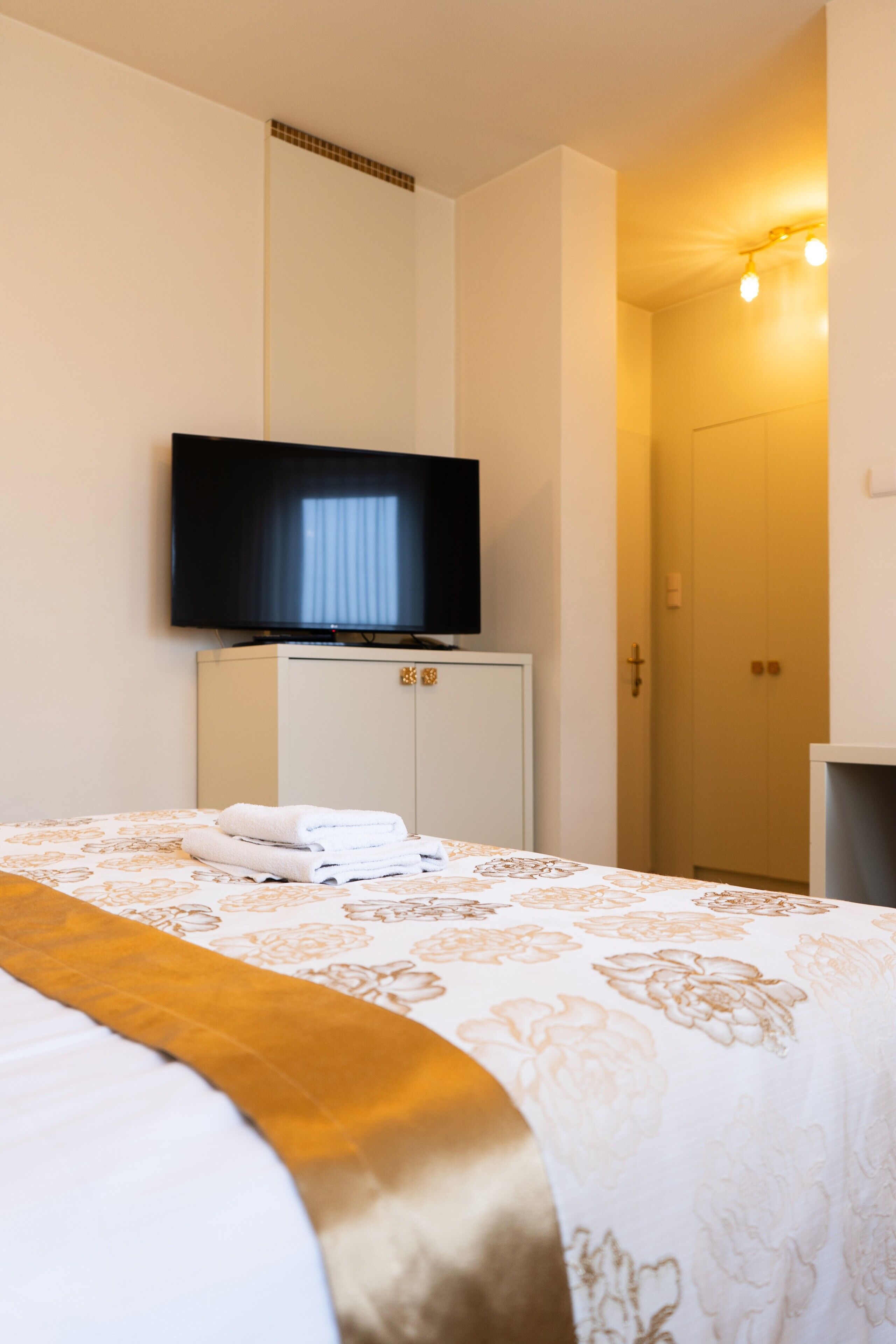A hotel room with a bed, a television mounted on the wall, and a wardrobe.