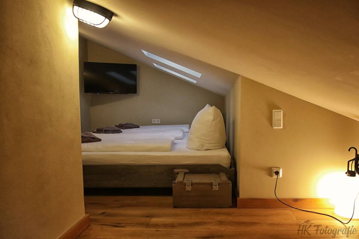 Ein kleines, gemütliches Schlafzimmer im Dachgeschoss mit einem Einzelbett, einem Flachbildfernseher und einer Holzkiste.