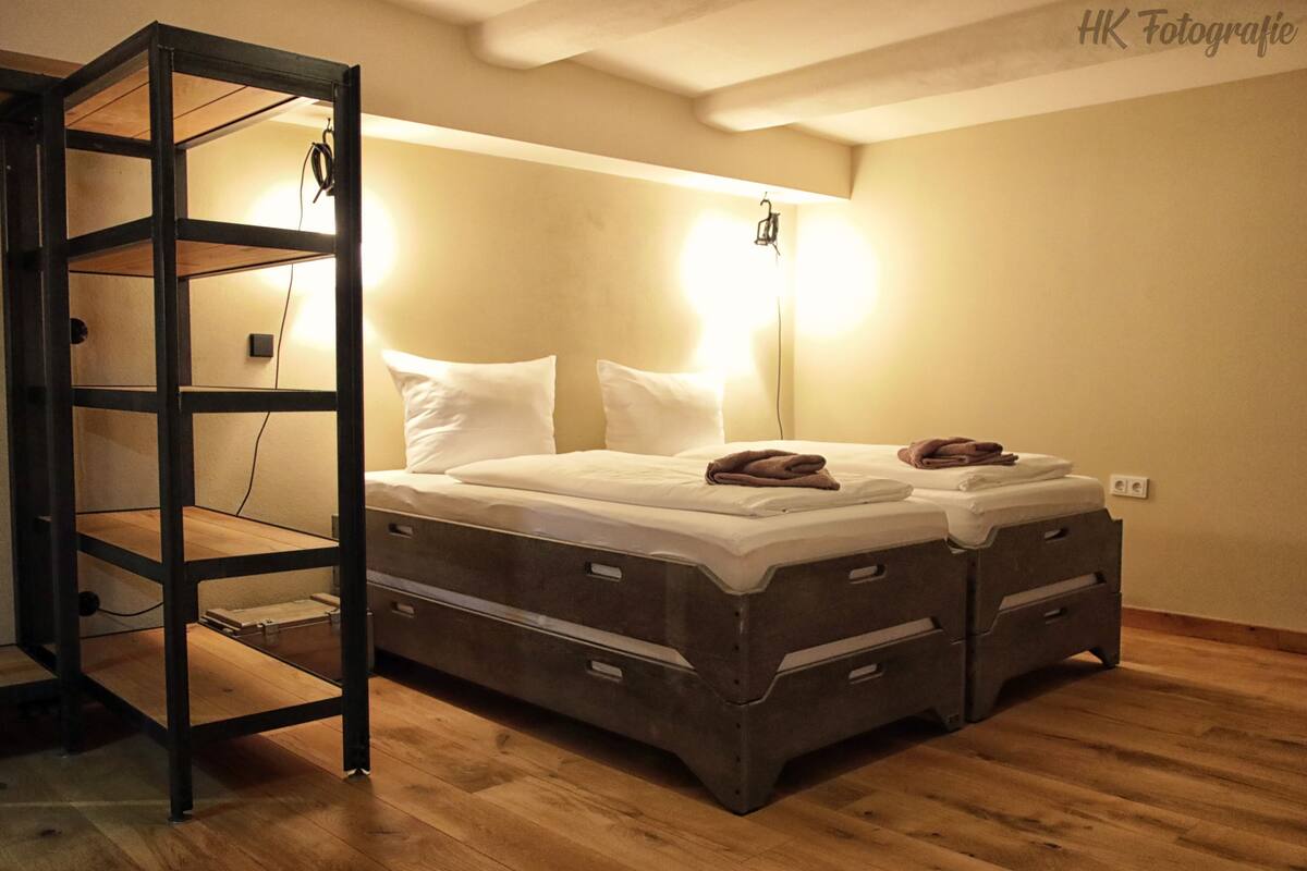 Ein Einzelbett mit Holzrahmen und Schubladen, ein Nachttisch und eine an der Wand befestigte Leuchte.