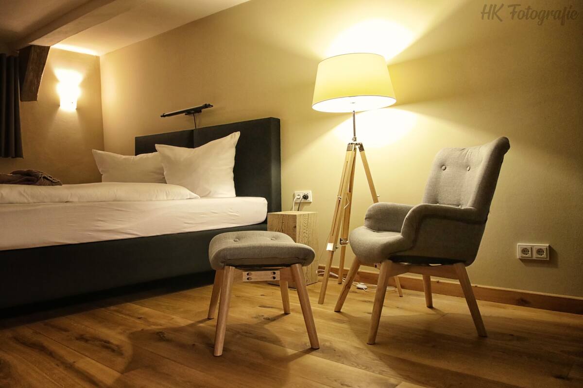 Ein Hotelzimmer mit einem Bett, einer Stehlampe, einem Sessel und einem kleinen Hocker.