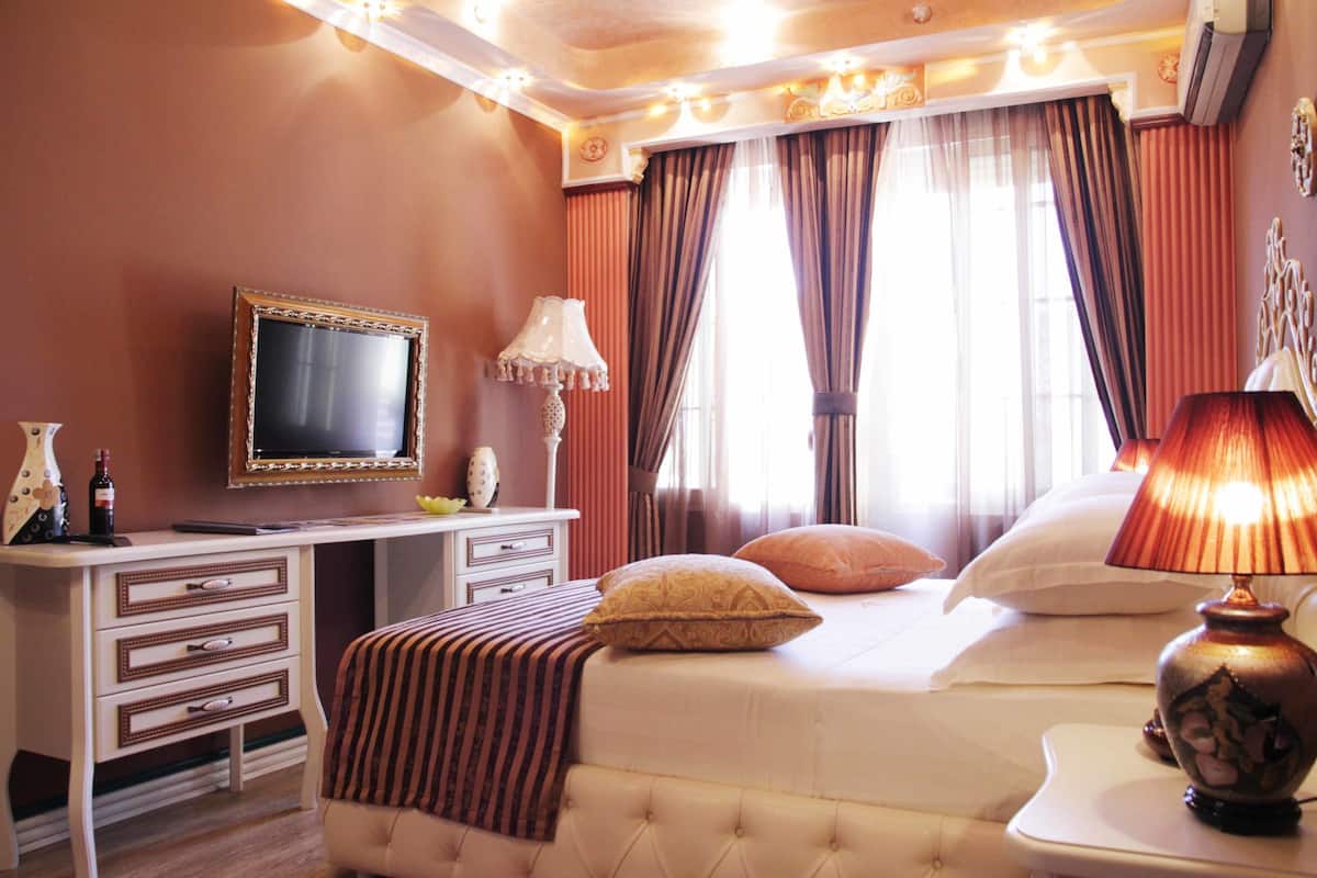 A hotel room with a bed, a desk with a television, a lamp, and a dresser.