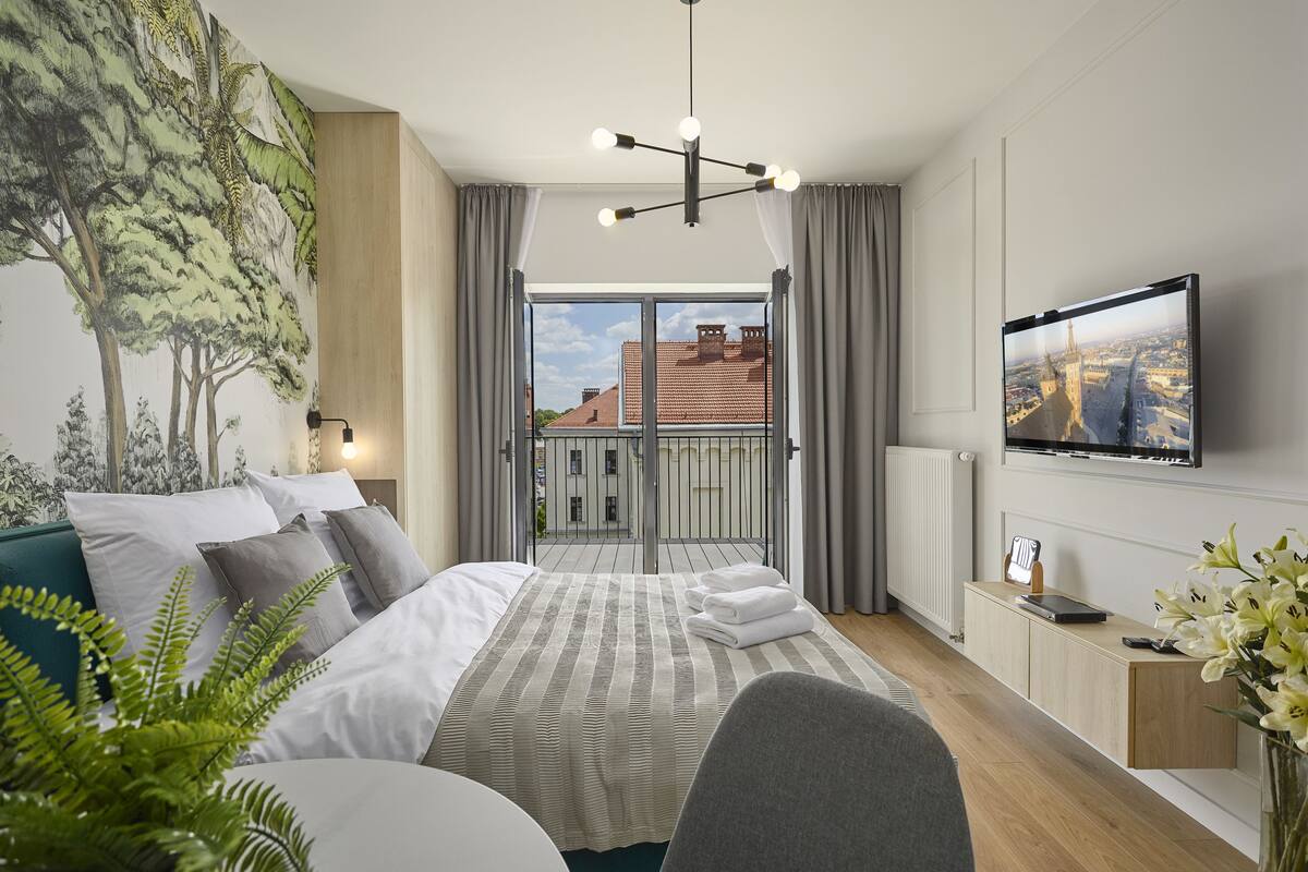 A modern hotel room with a large bed, a TV, a balcony with a city view, and a mural on the wall.