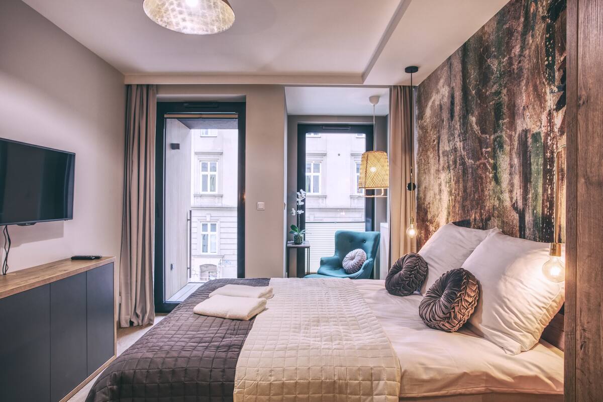 A modern hotel room with a large bed, a flat-screen TV, and a view of the city through the window.