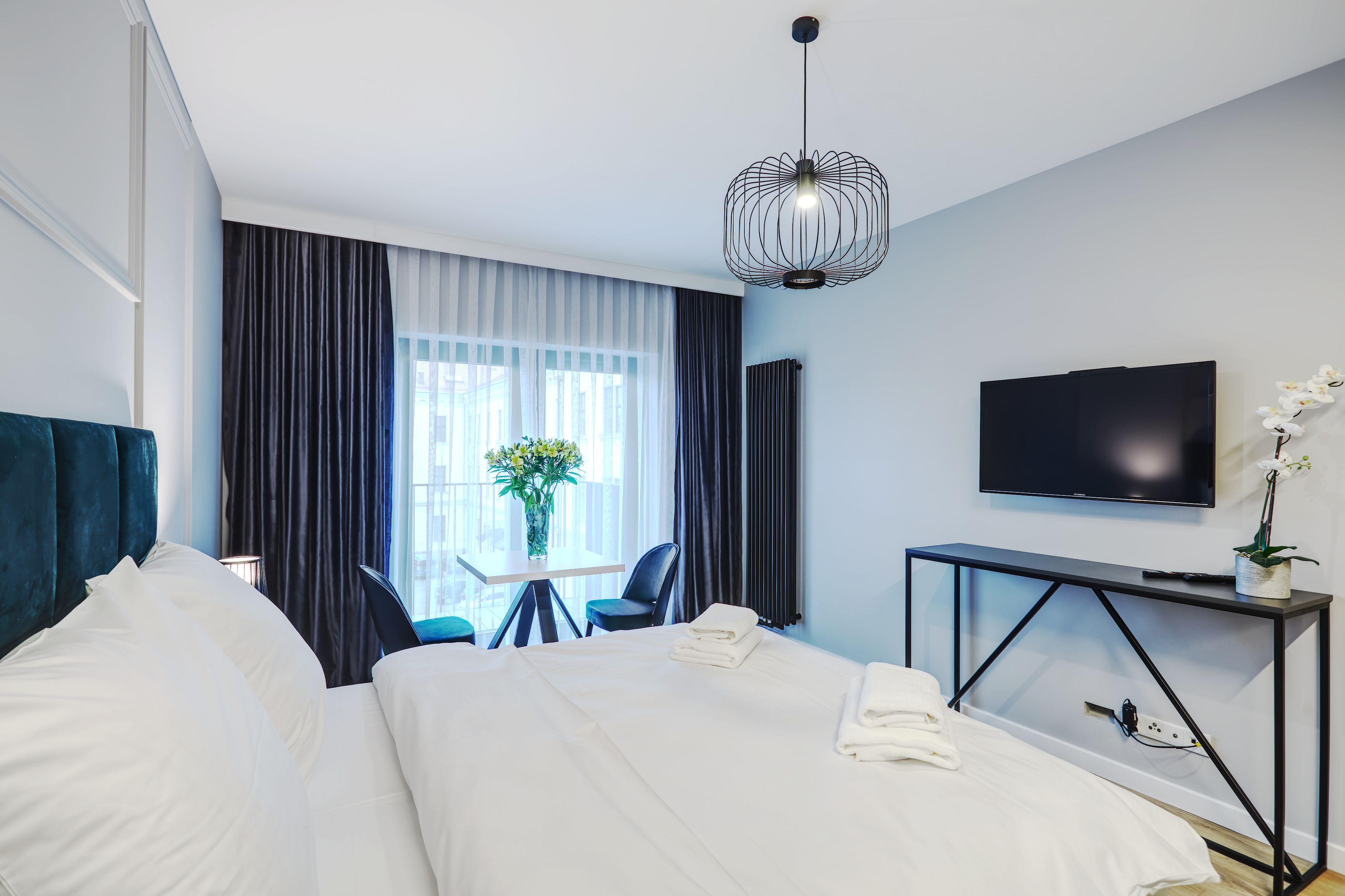 A hotel room with a bed, a desk, a chair, a TV, and a window with curtains.