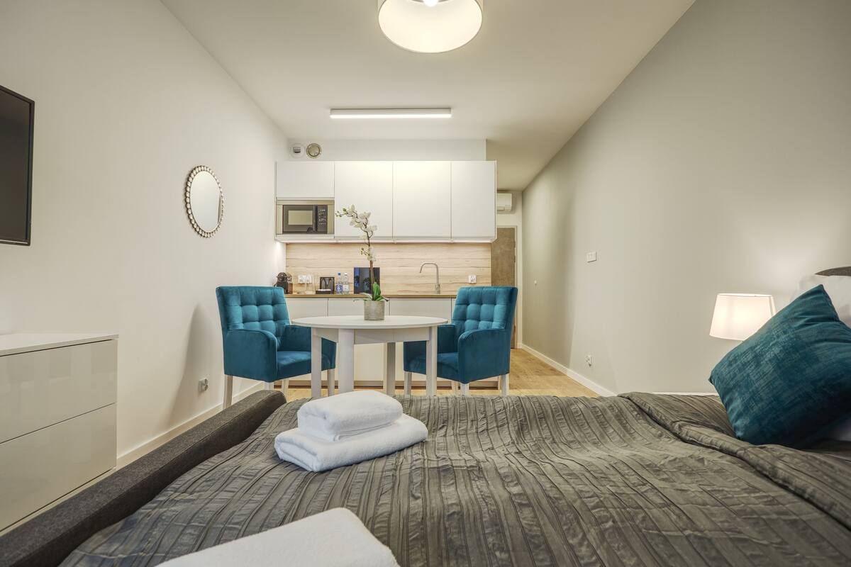 A modern hotel room with a bed, a small table, two chairs, a microwave, and a sink in the kitchen area.