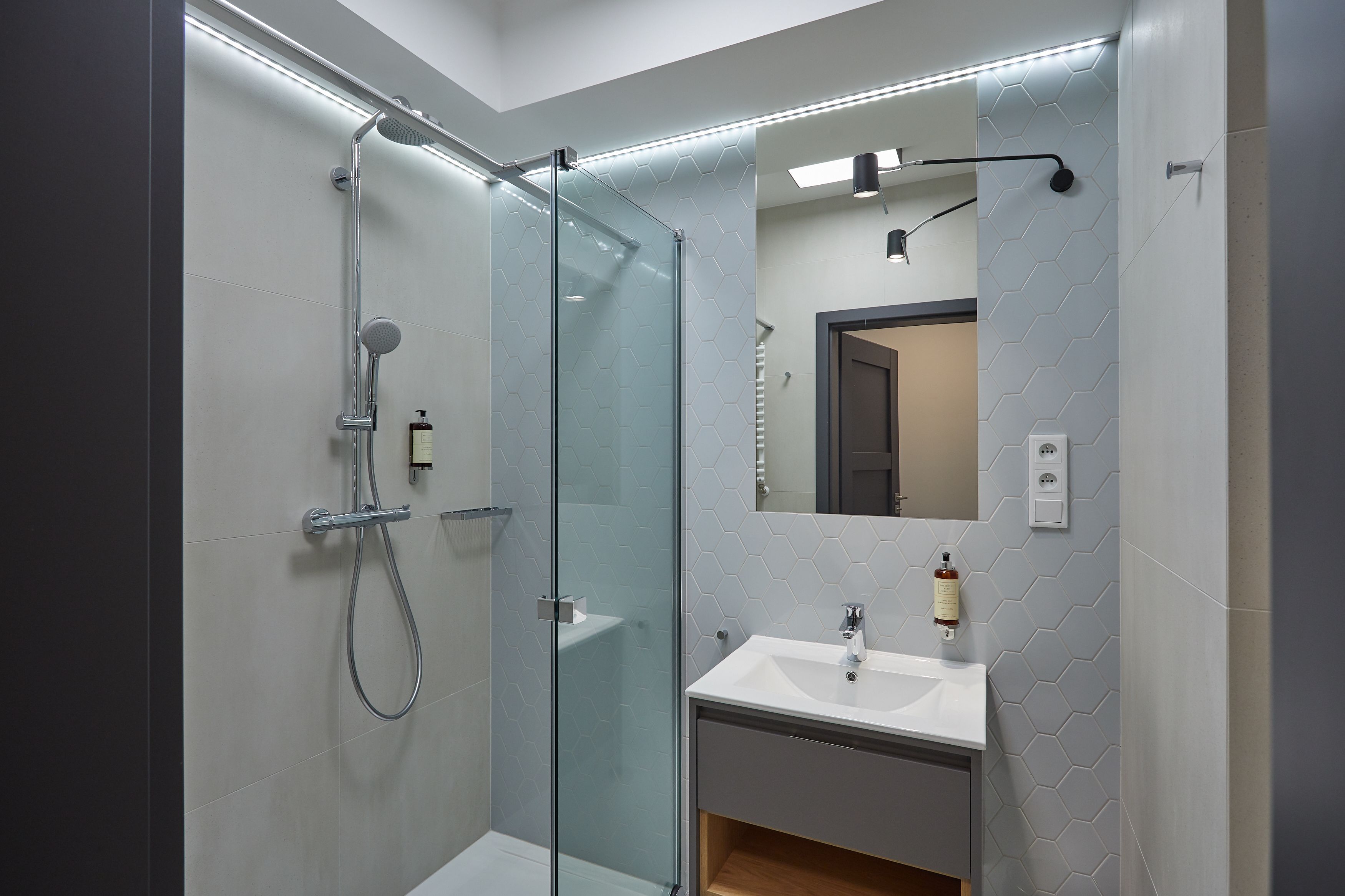 Une salle de bain moderne avec une douche à parois de verre, un lavabo avec un miroir et un luminaire fixé au mur.