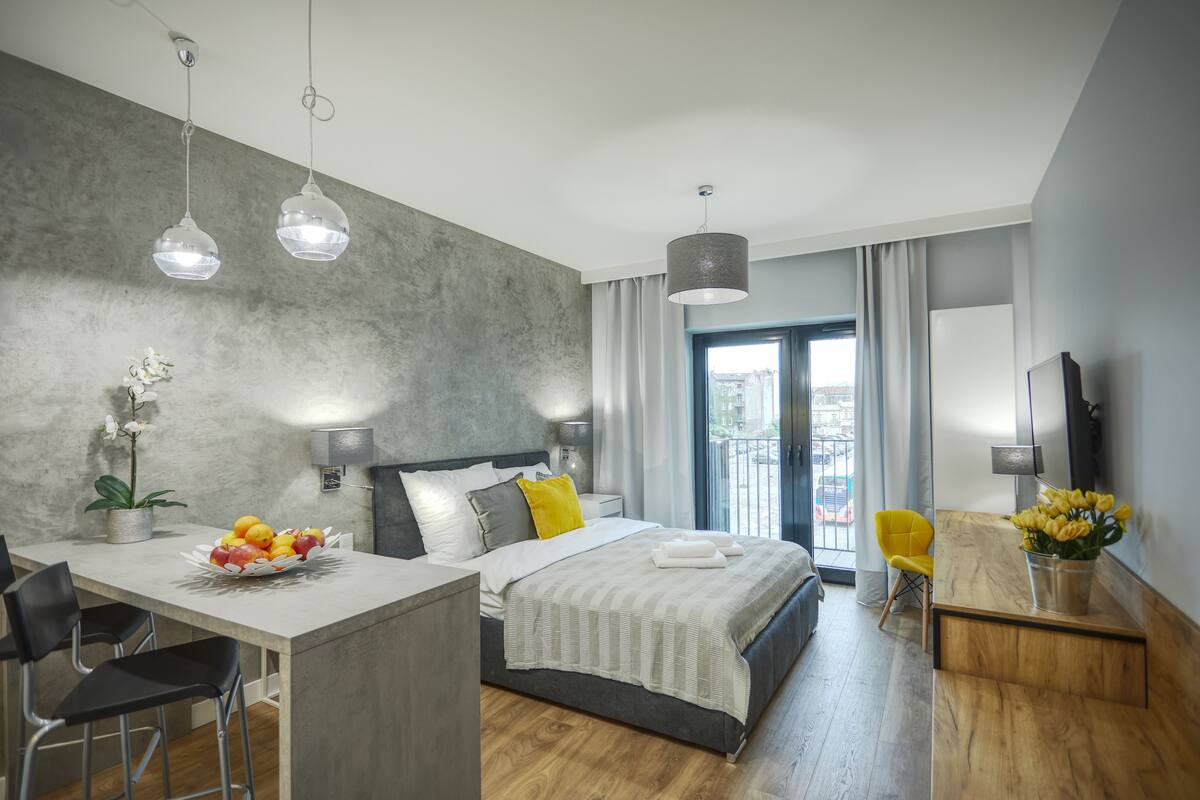 A modern hotel room with a large bed, a dining area, and a view of the outdoors.