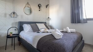 A neatly made bed with pillows, a bedside table with a cup and a bowl, and a small plant on a chair. - Royal haneviim Boutique palace (Jerusalem)