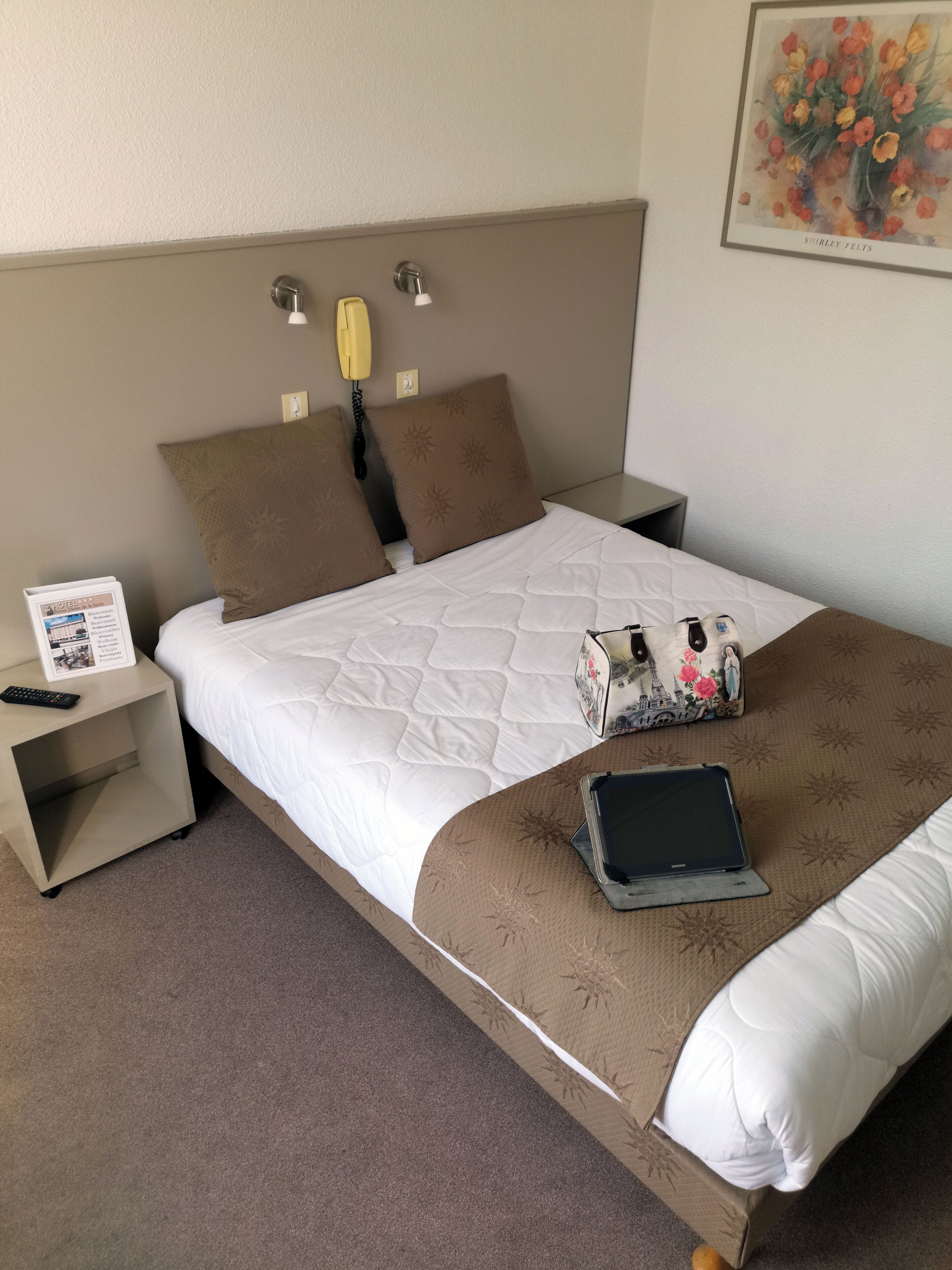 Camera d'albergo con un letto, comodini, una lampada, un quadro e un cartello.