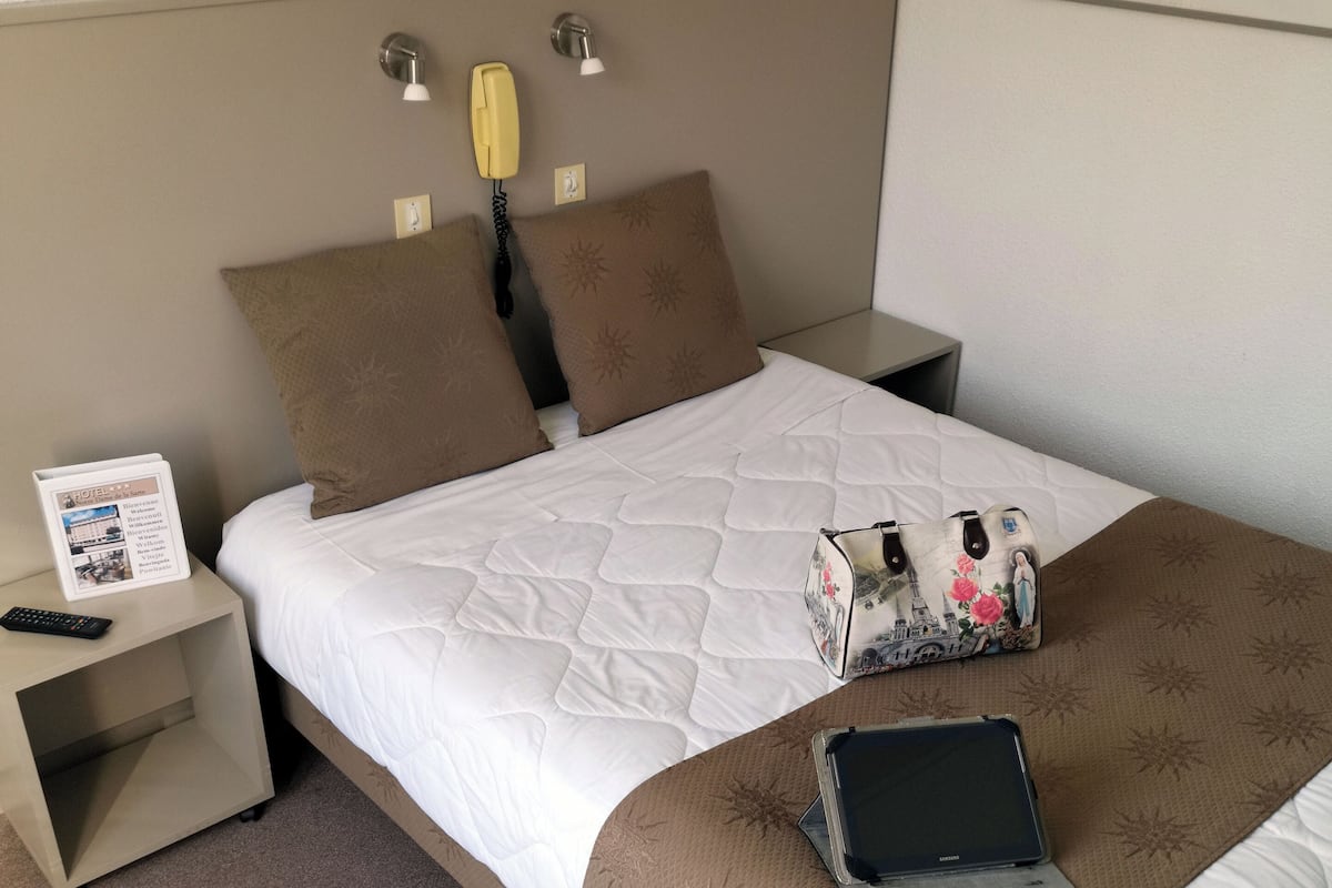 A hotel room with a bed, bedside tables, a lamp, a painting, and a sign.
