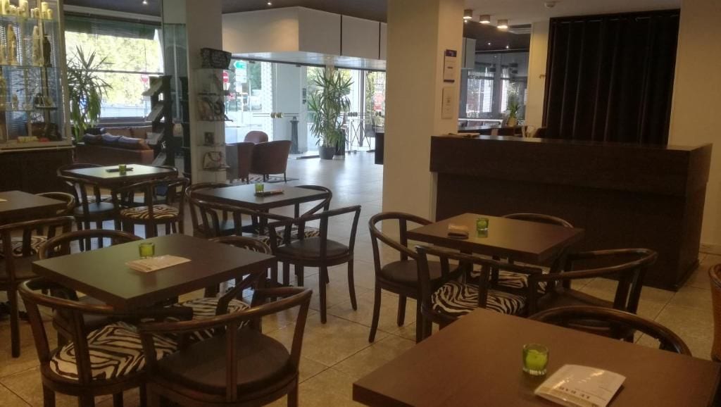 A restaurant with multiple tables and chairs, a reception desk, and a view of the street outside.