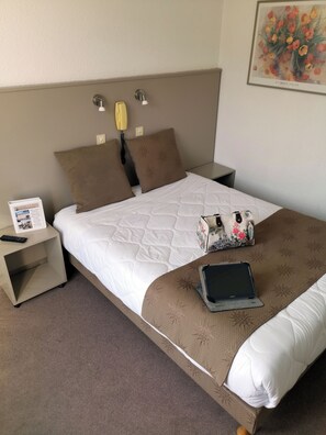 Una habitación de hotel con cama, mesitas de noche, una lámpara, un cuadro y un cartel.